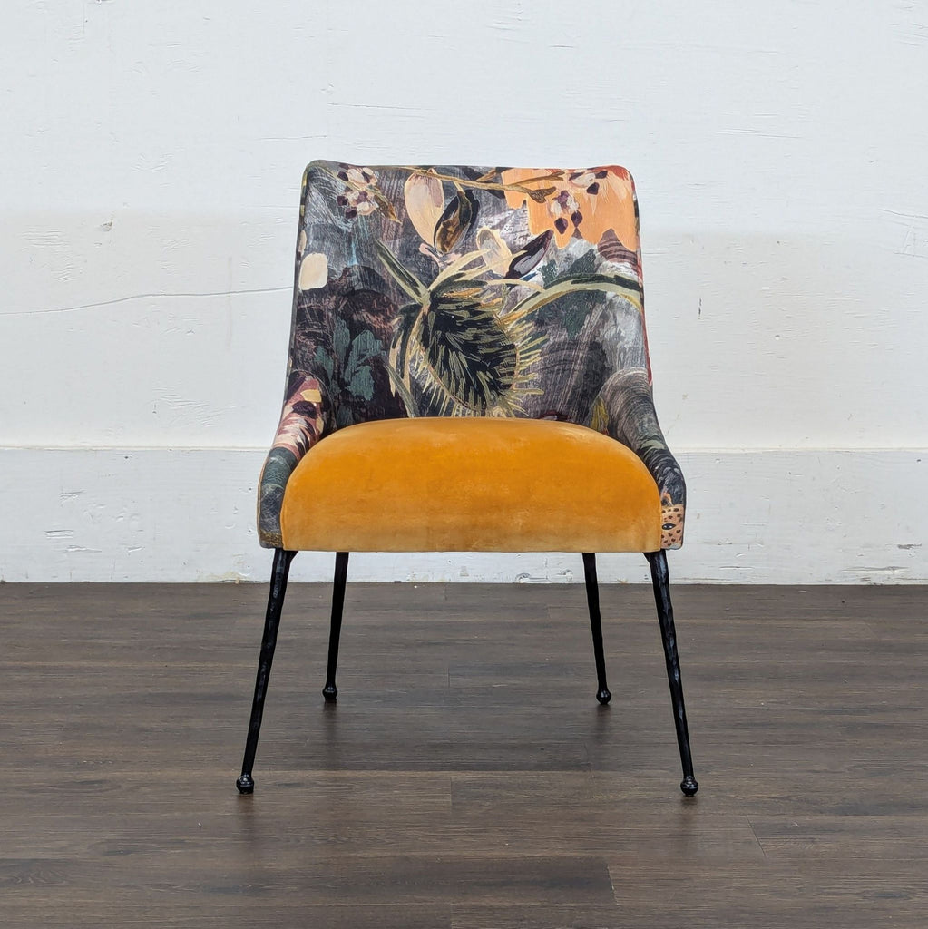 Front view of a lounge chair with a mustard yellow seat, floral upholstery, and slim black legs on wooden floor.