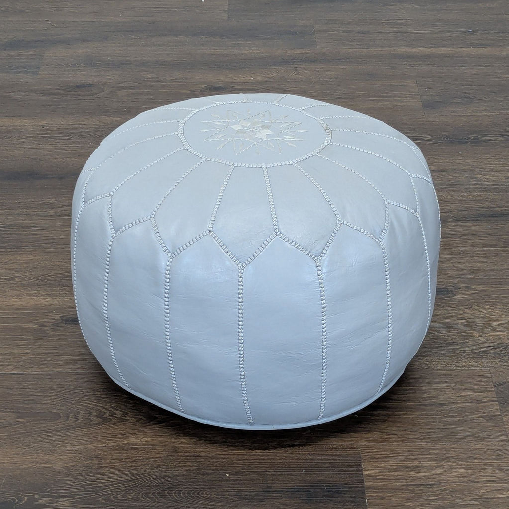 Light gray leather pouf from Reperch with stitched panels and a decorative star pattern, on a wooden floor.  