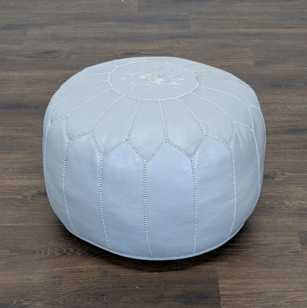 Light gray leather pouf from Reperch with stitched panels and a decorative star pattern, on a wooden floor.  