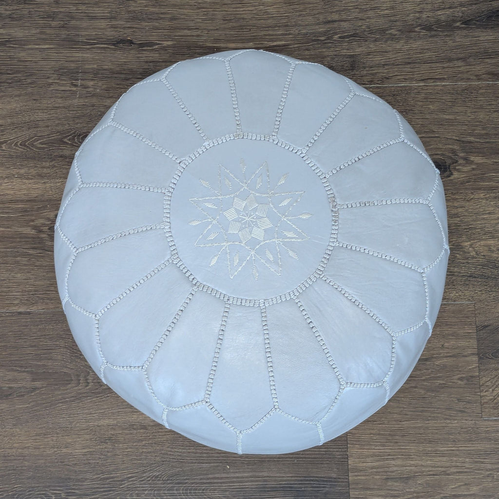 Top view of a round Reperch ottoman showing intricate stitched star design and panel detailing on gray leather.  