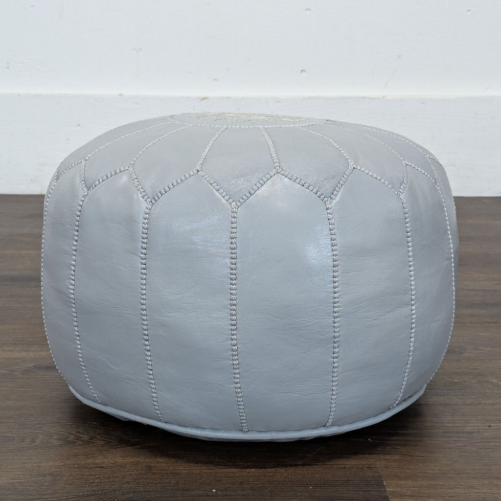 Side view of a Reperch pouf in light gray leather, featuring visible stitched segments and a soft, rounded shape.