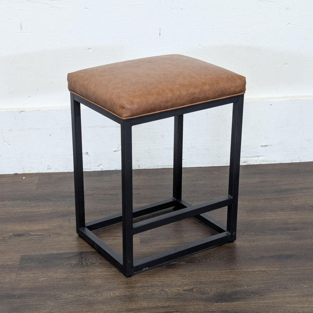Angled view of a Reperch stool, showing brown leather-like cushion and sturdy black metal frame construction.