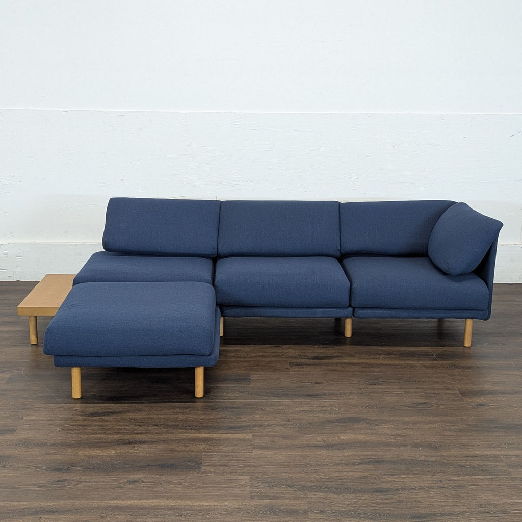 2. Burrow sectional sofa in navy blue fabric with wooden legs and integrated side table, set on wood floor.