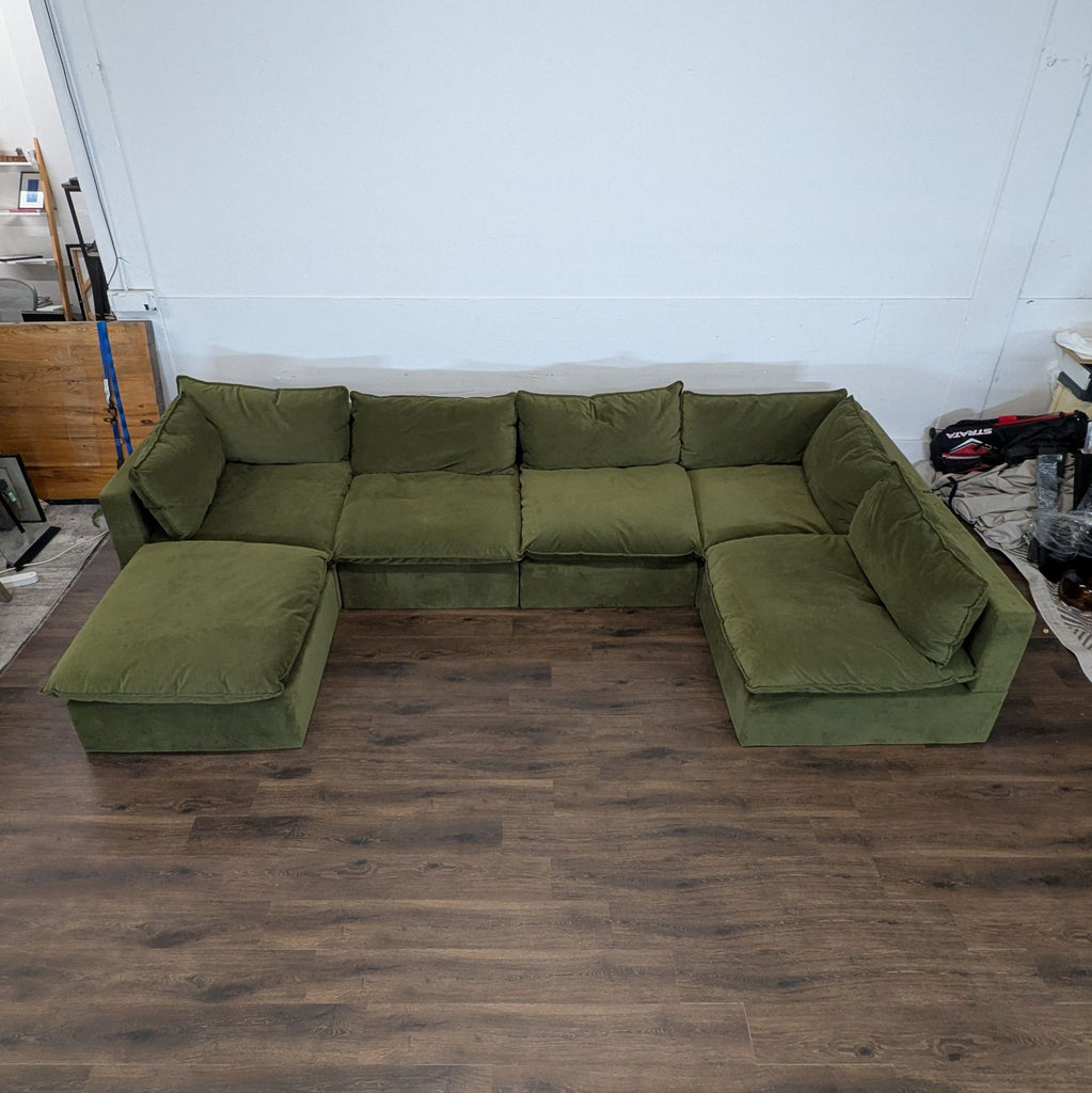 Olive green sectional sofa by sofa brand, arranged in an L-shape, shown in a spacious room with wood flooring.
