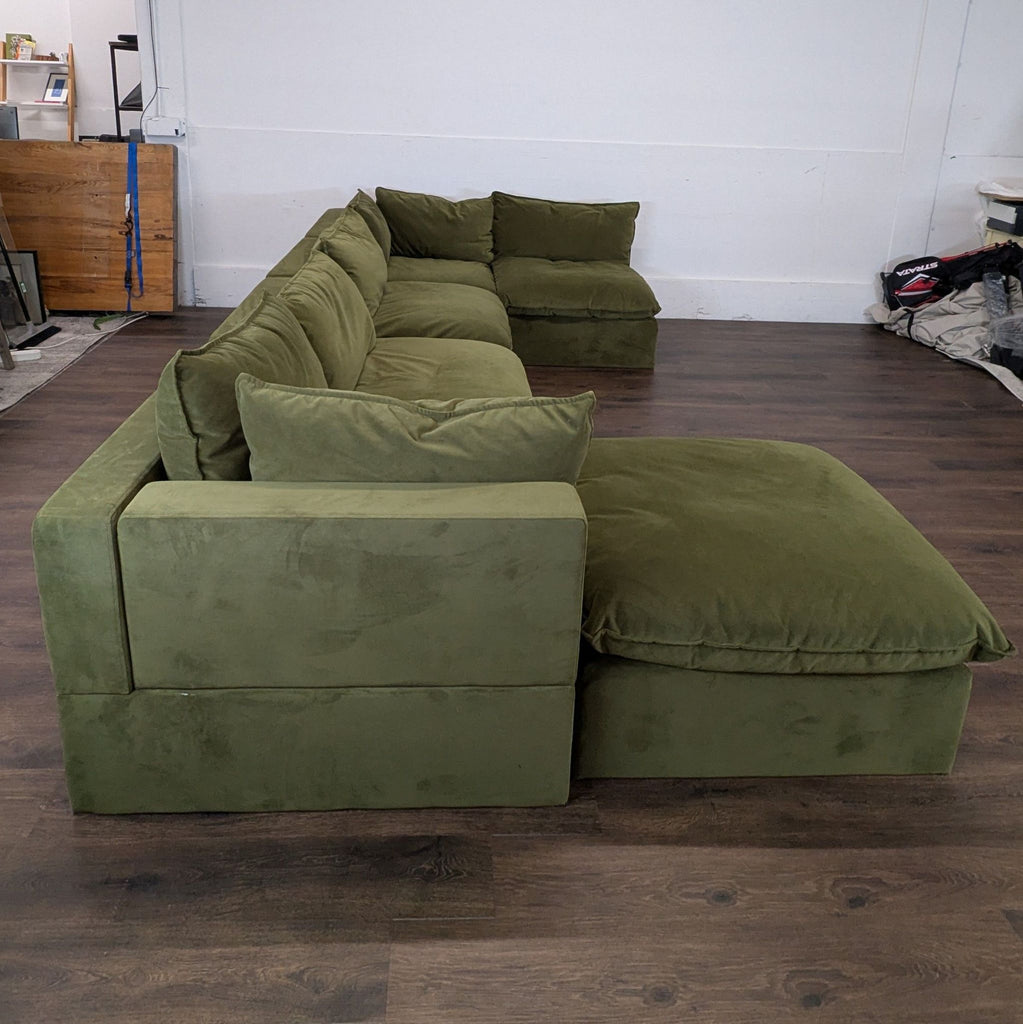 Side view of a green sectional sofa, highlighting deep cushions and good condition, on a dark wood floor.