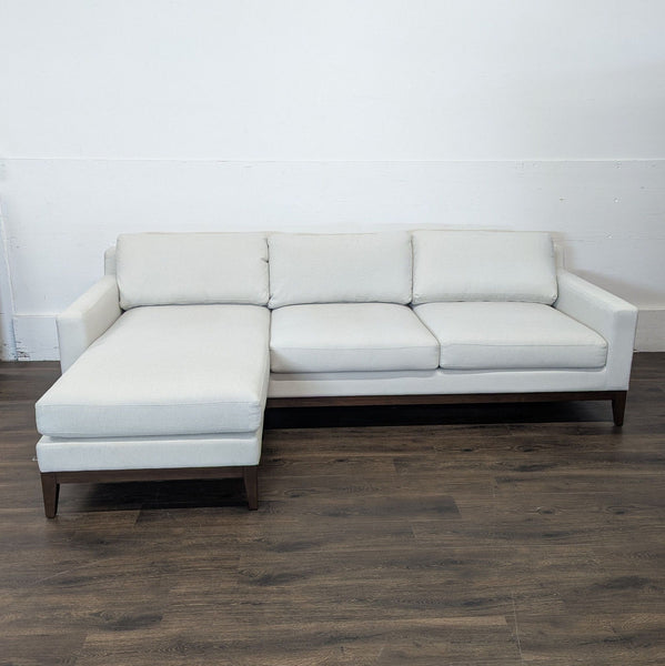 1. Front view of a Reperch sectional sofa with light fabric and dark wooden base, featuring a chaise lounge.  