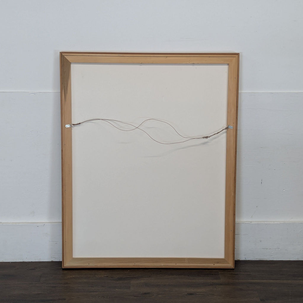3. Back view of a Reperch framed drawing, showing wooden frame and attached hanging wire, against a plain wall.