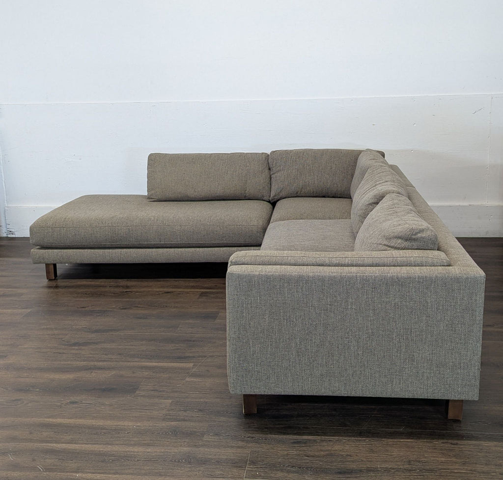 3. Reperch sectional sofa in neutral gray fabric with low back and cushions, set on dark wood flooring against a white wall.