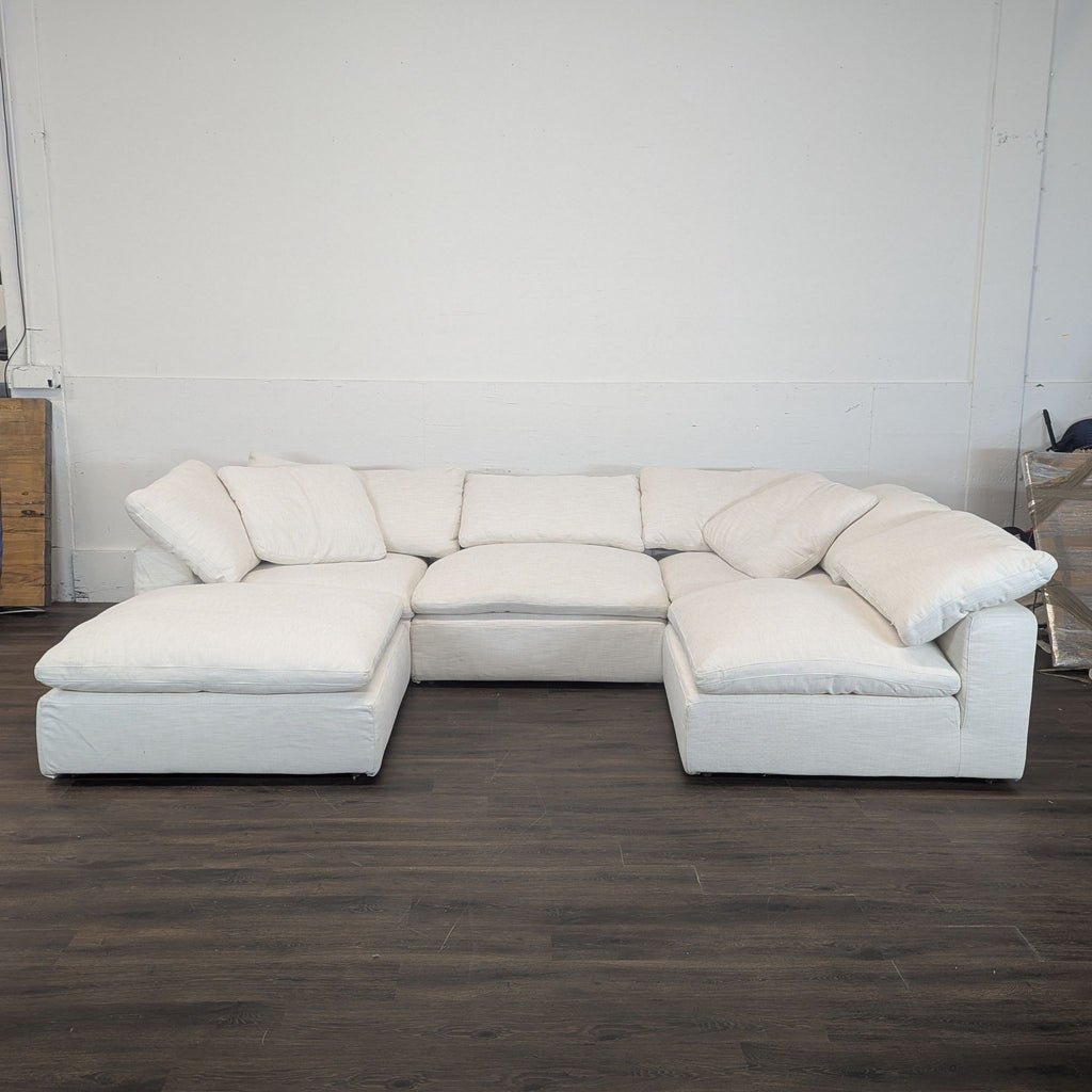 1. Restoration Hardware sectional sofa in light fabric, arranged in an L-shape against a white wall on dark flooring.  