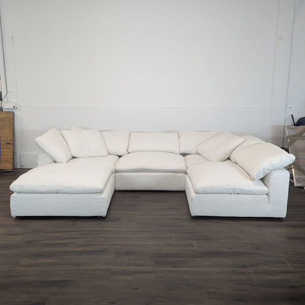 1. Restoration Hardware sectional sofa in light fabric, arranged in an L-shape against a white wall on dark flooring.  