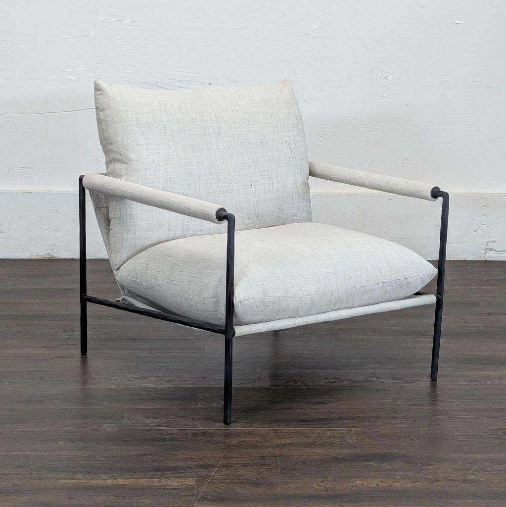 3. Side angle of a Crate and Barrel accent chair in light fabric, with a metal frame and wooden floor background.