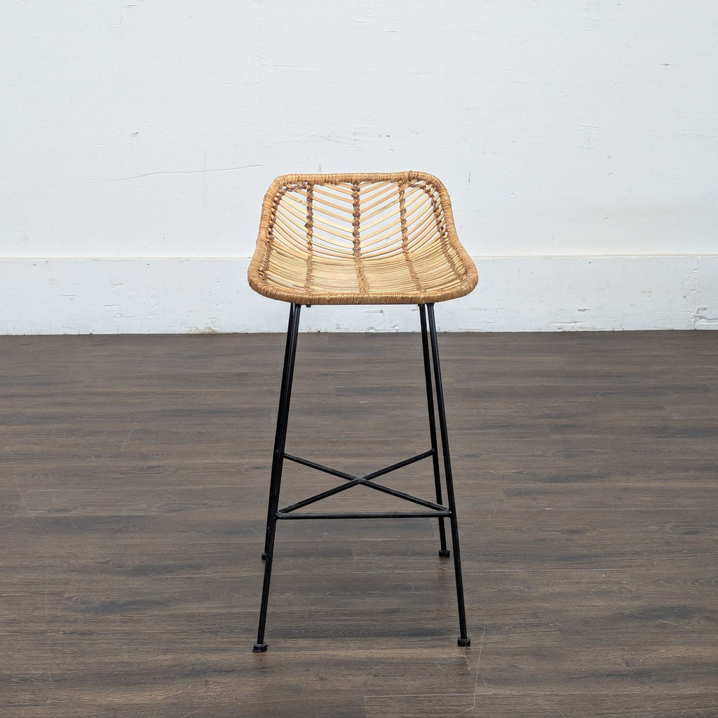 2. Single rattan bar stool with curved seat and black metal legs on a dark wood floor, white wall background.