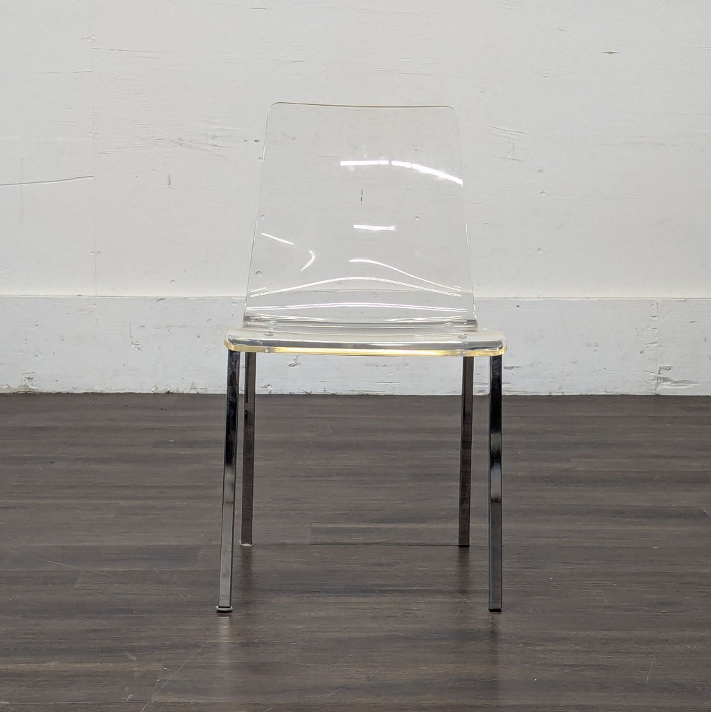2. Transparent acrylic dining chair with chrome legs placed on a dark wooden floor against a plain wall.