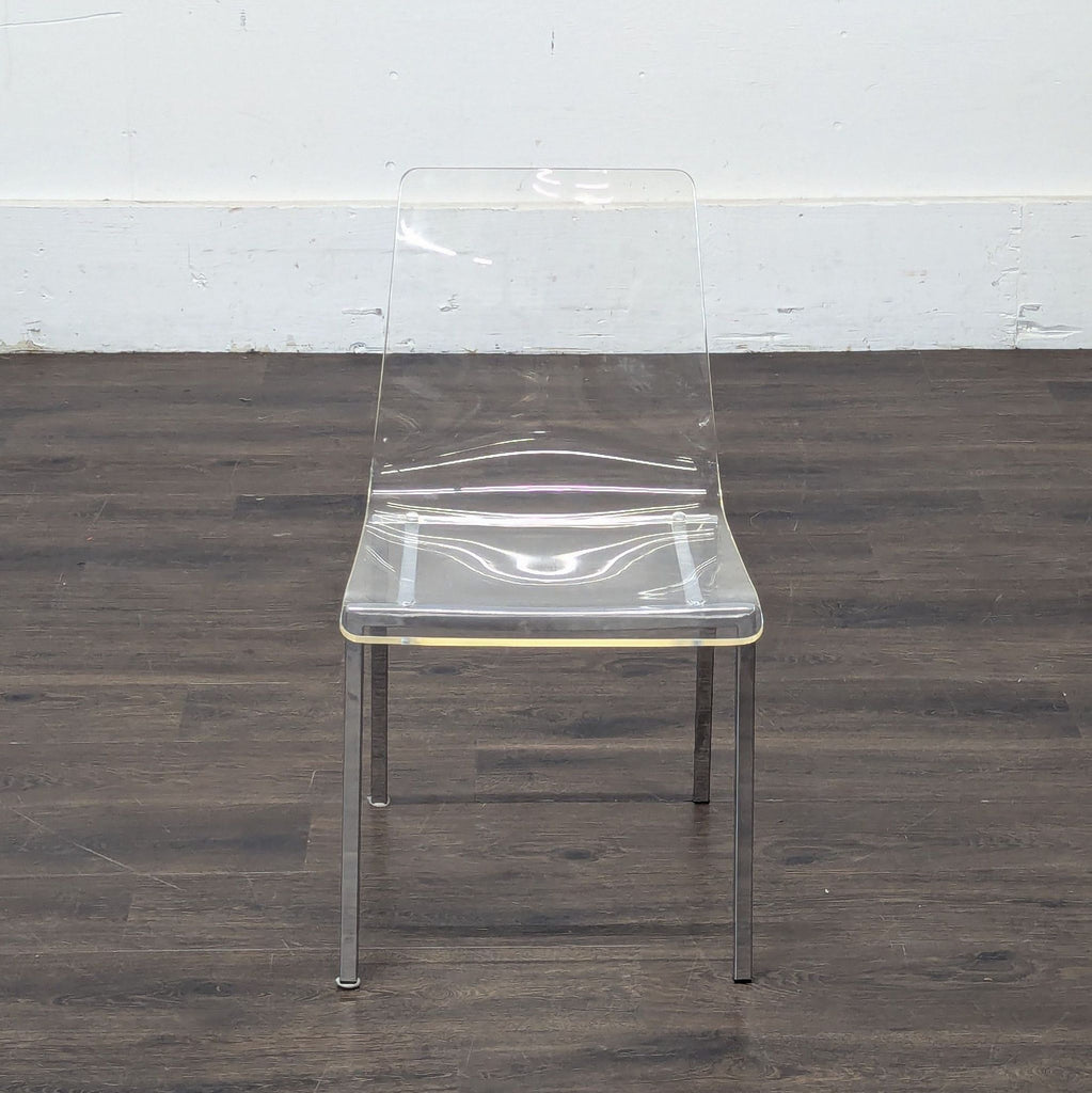3. Stylish clear plastic dining chair with a contoured seat and chrome legs on a dark hardwood floor.