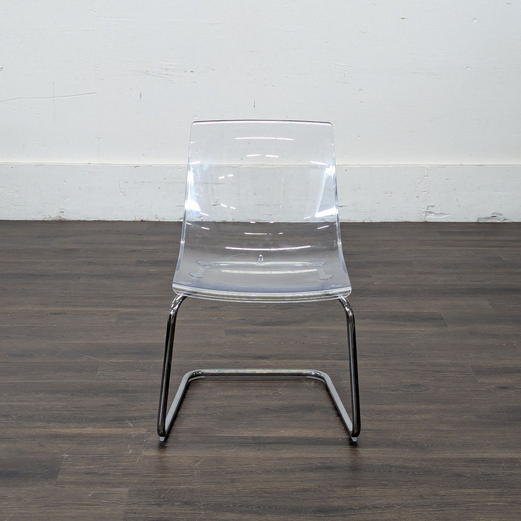 1. Clear acrylic dining chair with chrome legs from Ikea, shown on dark wood flooring against a white wall.