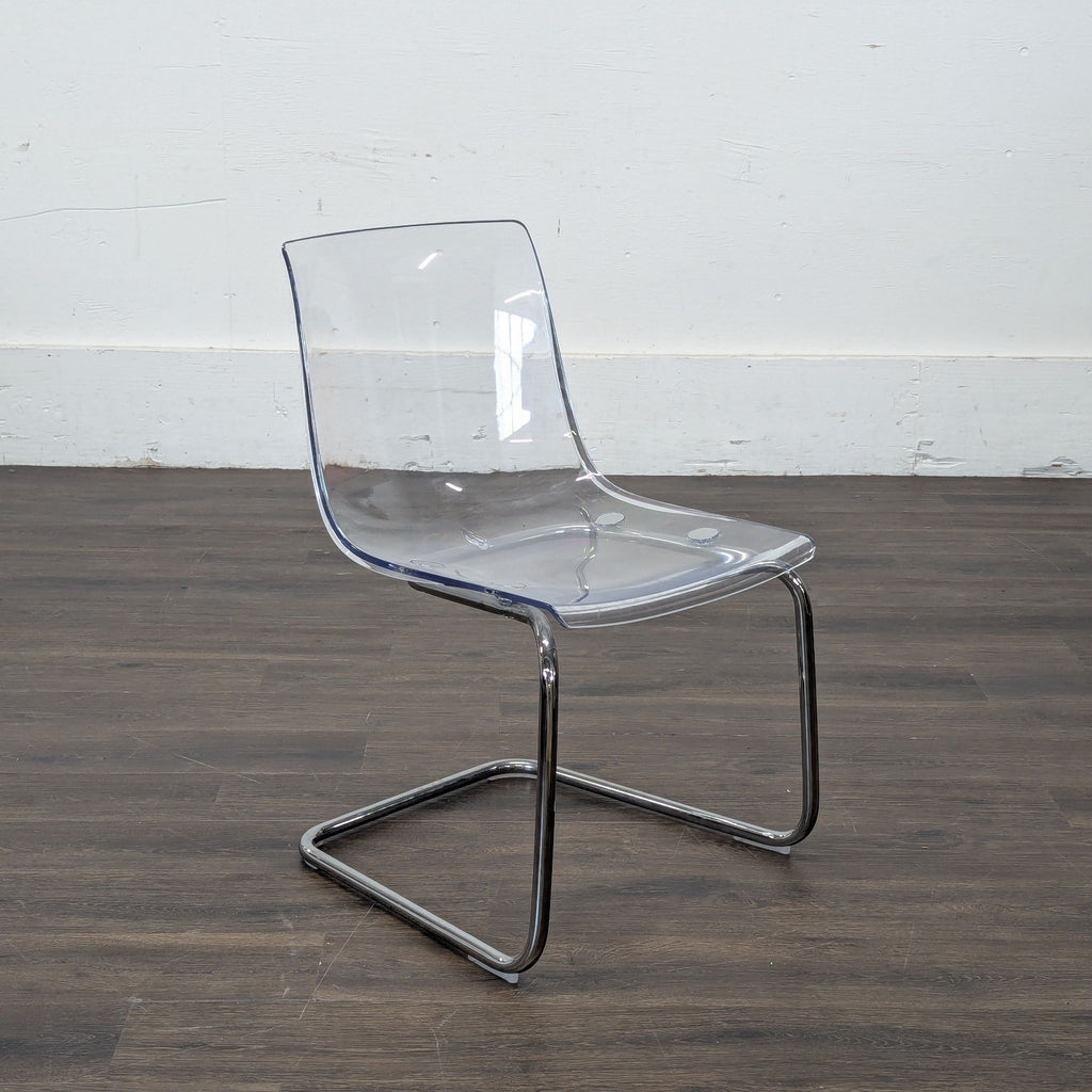 3. Modern clear Ikea dining chair with chrome frame, angled view on a dark wooden floor and plain white wall.