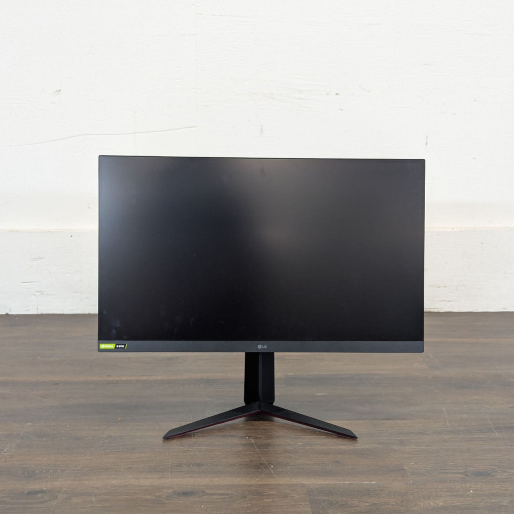 Front view of an LG UltraGear widescreen monitor with a slim bezel and V-shaped stand on a wooden floor.