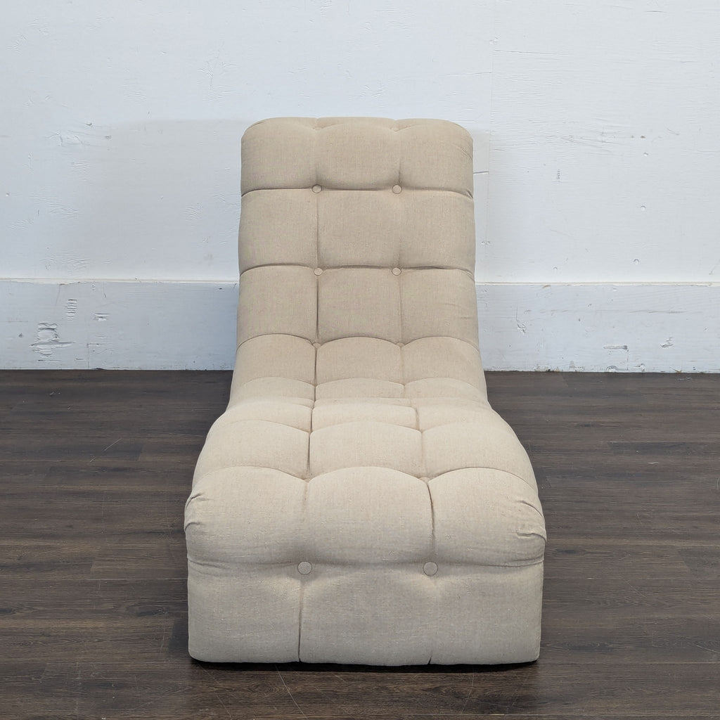 Beige tufted lounge chair with button details, unwrapped and displayed on a dark wood floor against a white wall.