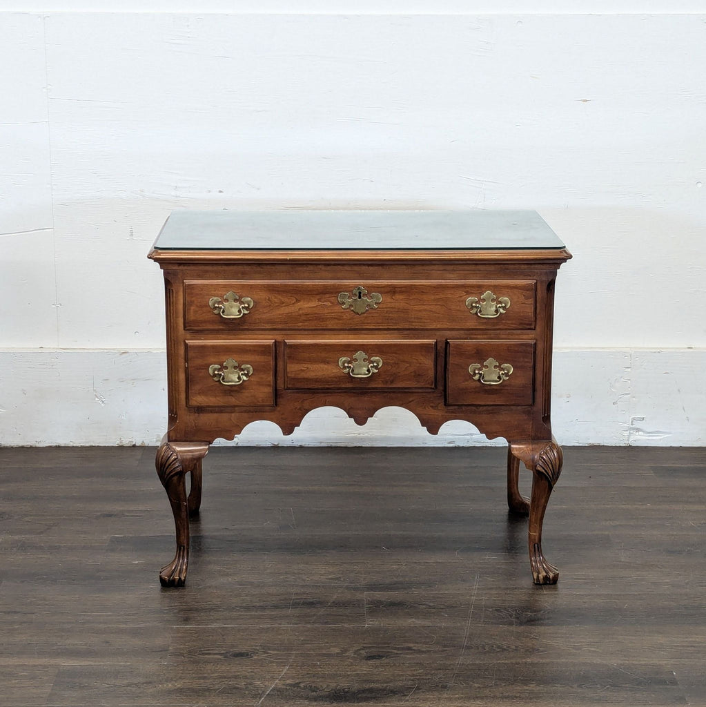 Elegant three-drawer sideboard with brass handles, paw feet, scalloped apron, and protective glass top.