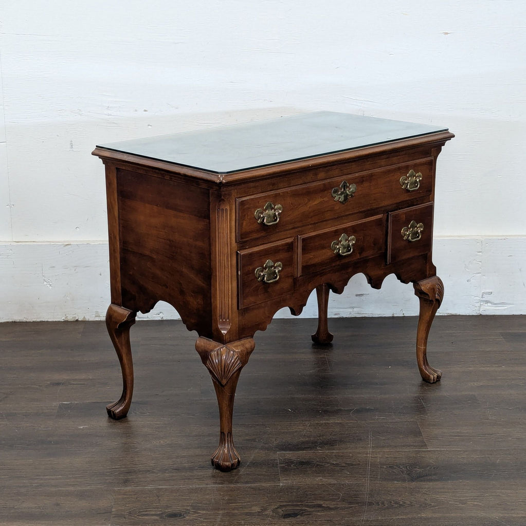 Classic chest with scalloped base, brass pulls, ornate legs ending in paw feet, and a glass top for protection.