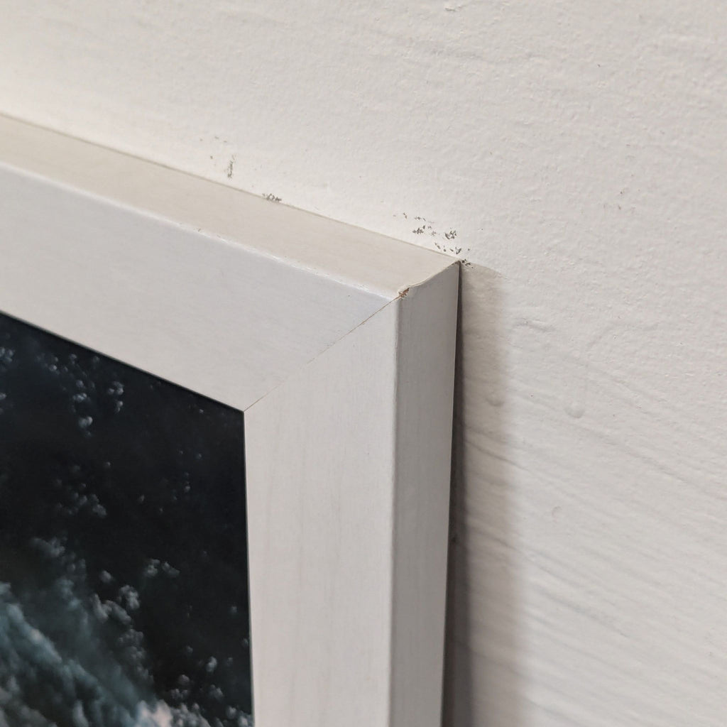 Close-up of the white corner frame on the ocean waves print, highlighting slight wear and detail in the finish.