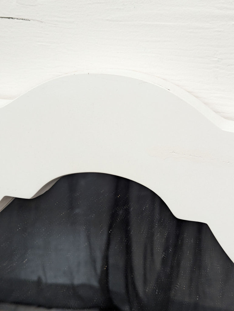 3. Detailed view of the upper curved section of the mirror’s white frame, showing minor surface marks.
