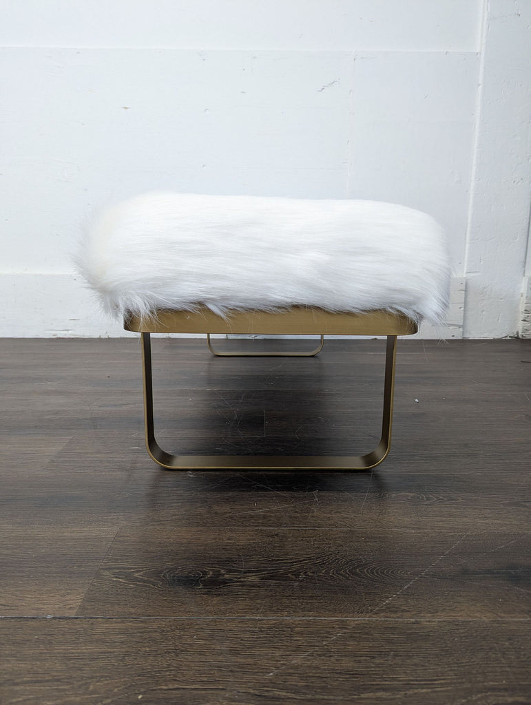 Luxurious faux fur ottoman with gleaming gold sled base, designed by Restoration Hardware for elegant seating.