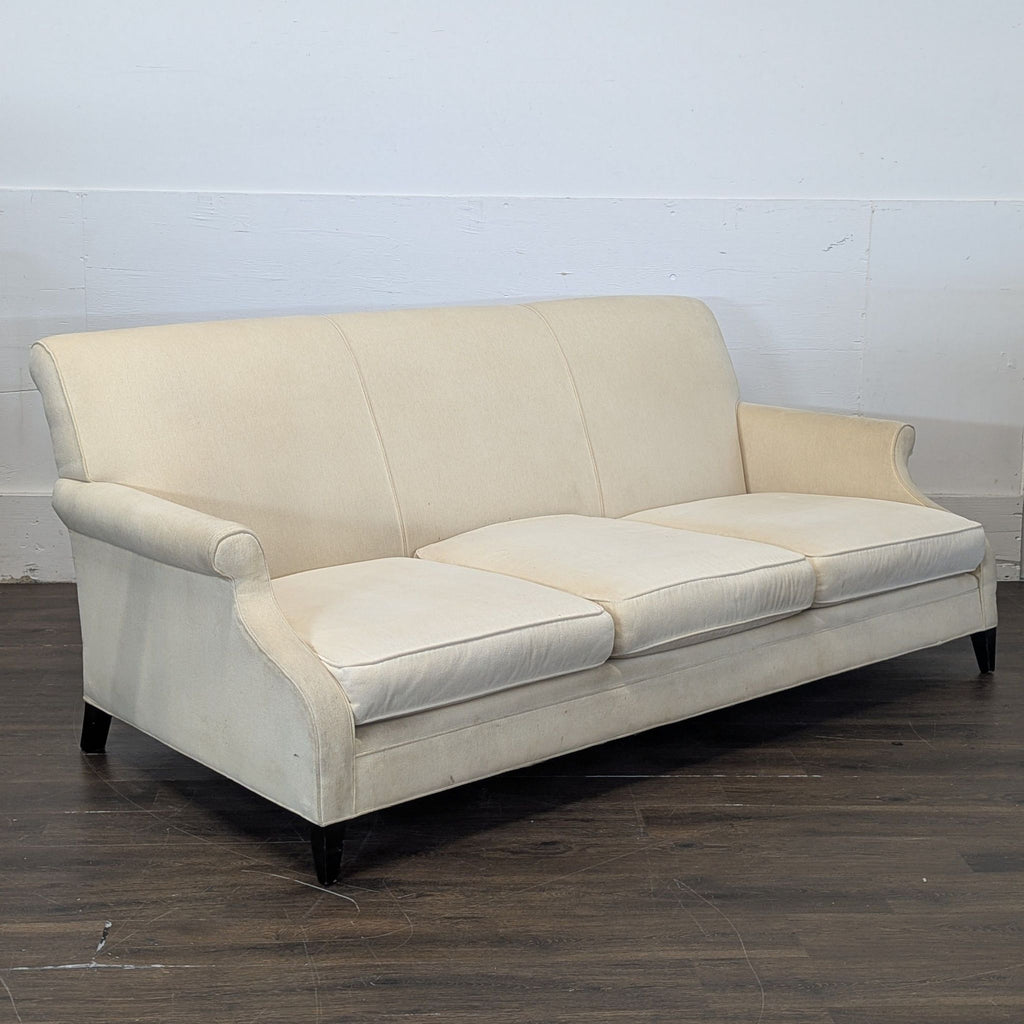 3. Side angle of a Restoration Hardware cream 3-seat sofa with elegant rolled arms and wooden legs on wood flooring.