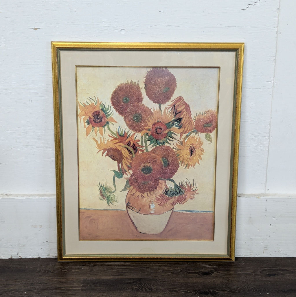 2. Van Gogh sunflower print in a gold frame, leaning against a white wall and dark wood floor.