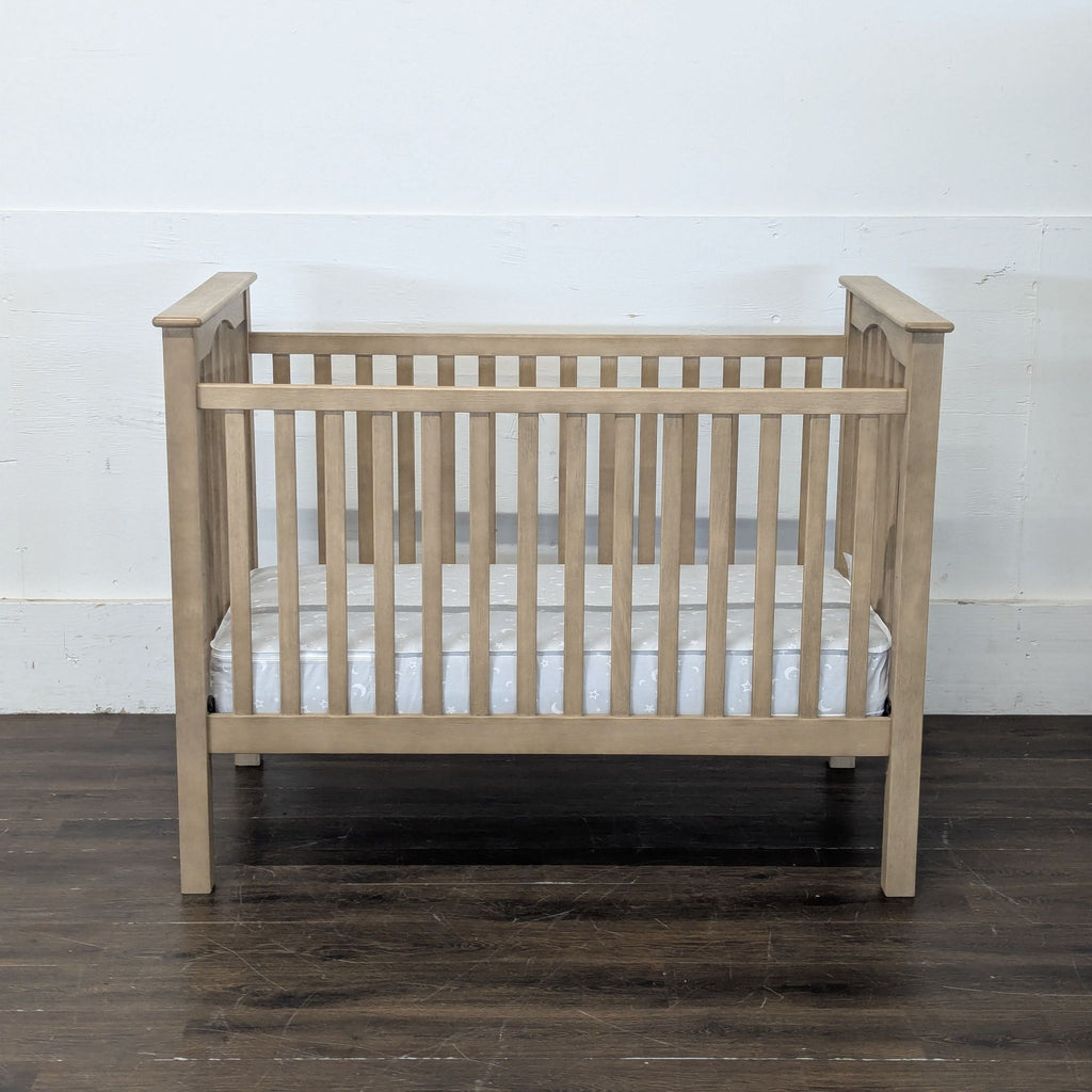 Natural wood Pottery Barn Kids crib with slatted sides, mattress included, shown on hardwood floor front view.  