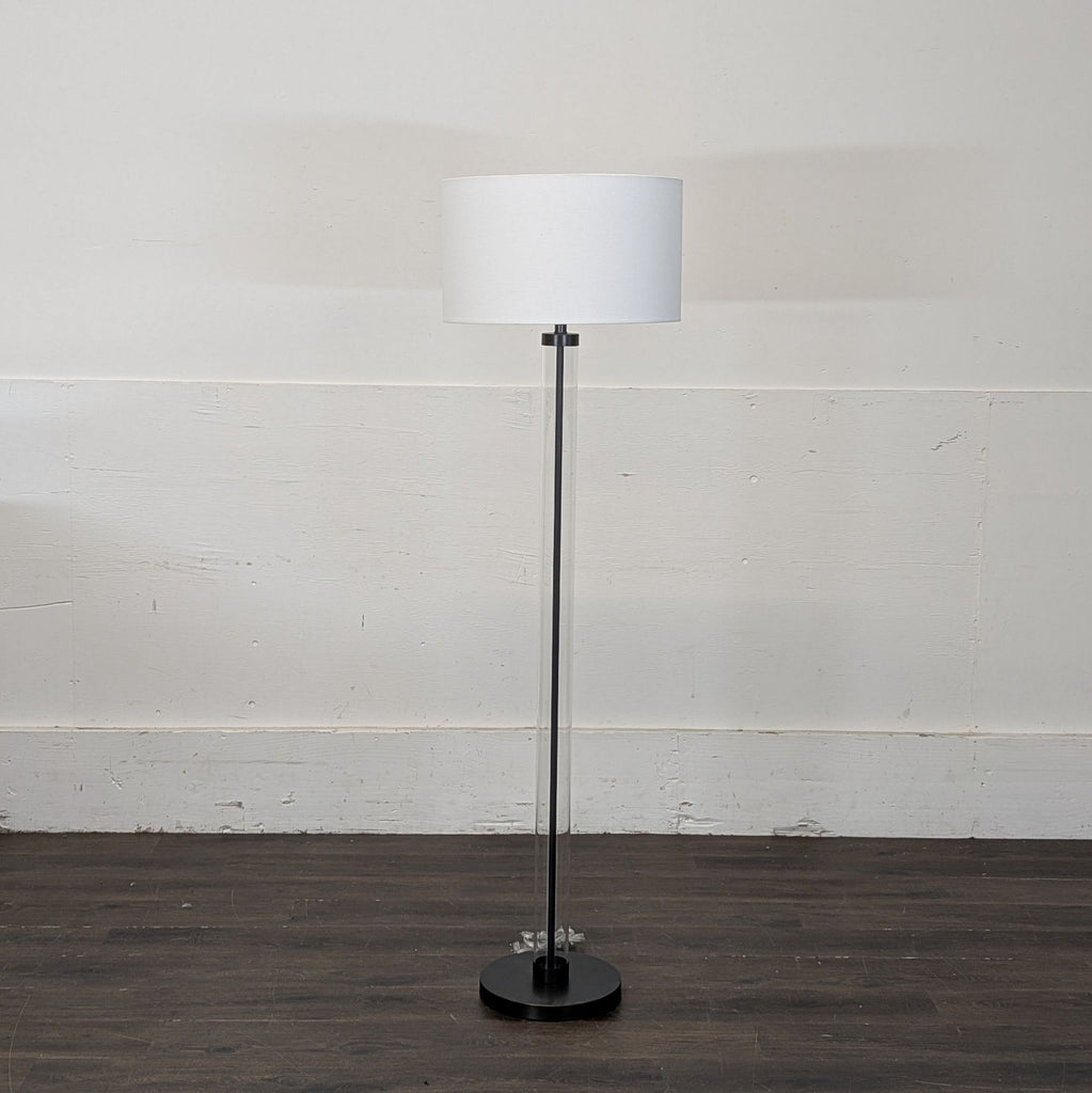 2. Modern Arhaus floor lamp featuring a white drum shade and clear base, placed on dark wood flooring.  