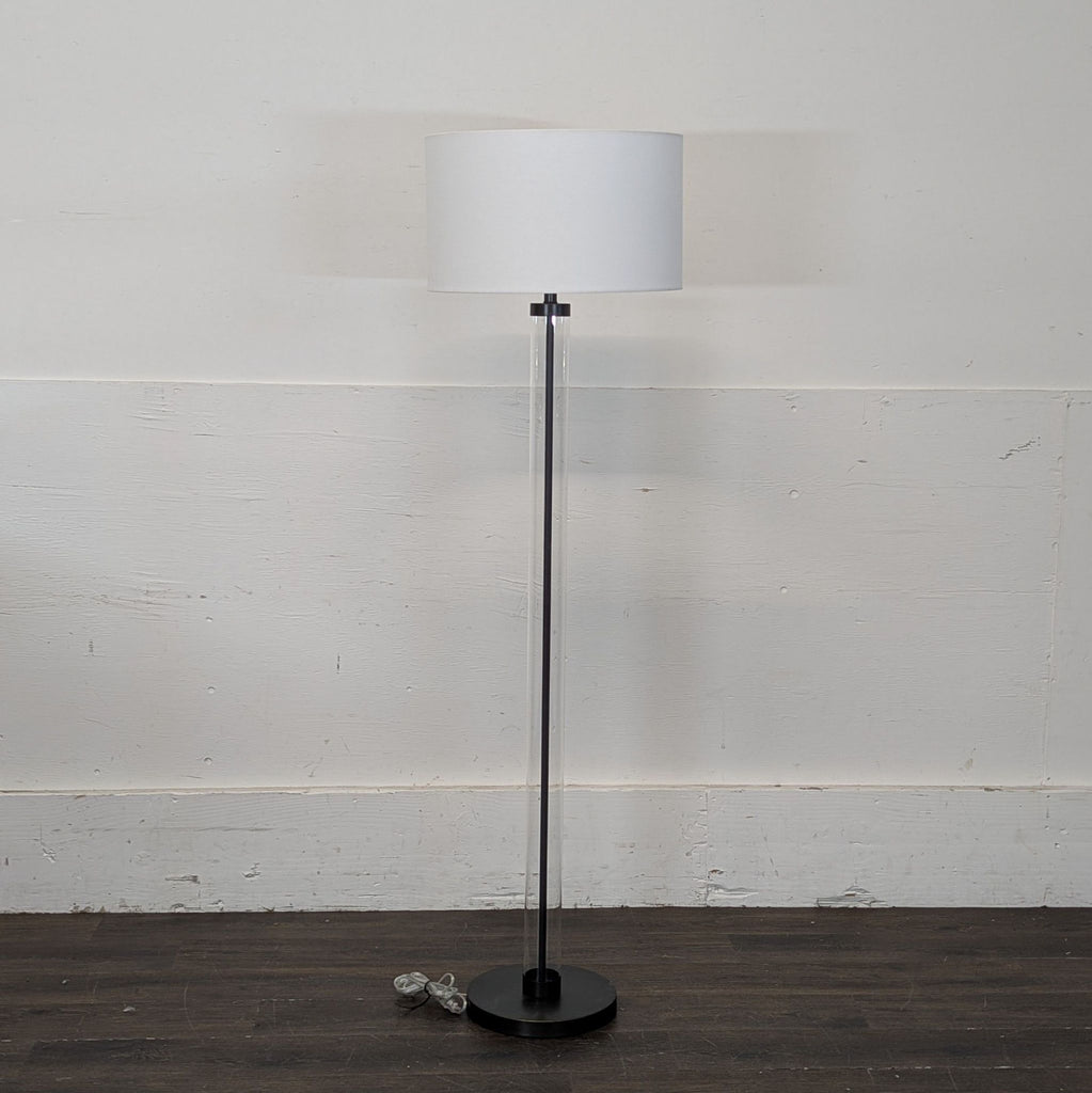 3. Minimalist Arhaus floor lamp with white shade and clear stand, shown against a plain wall in a bright room.