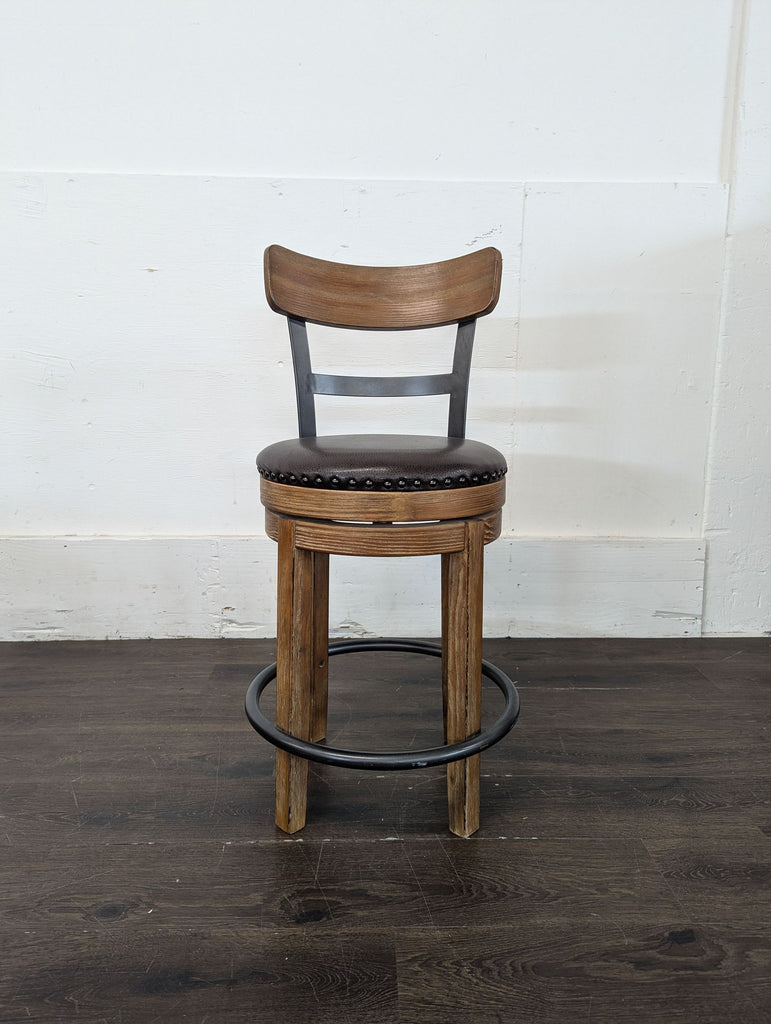 3. Wooden bar stool with a dark round padded seat, metal footrest, and curved backrest, placed near a wall.
