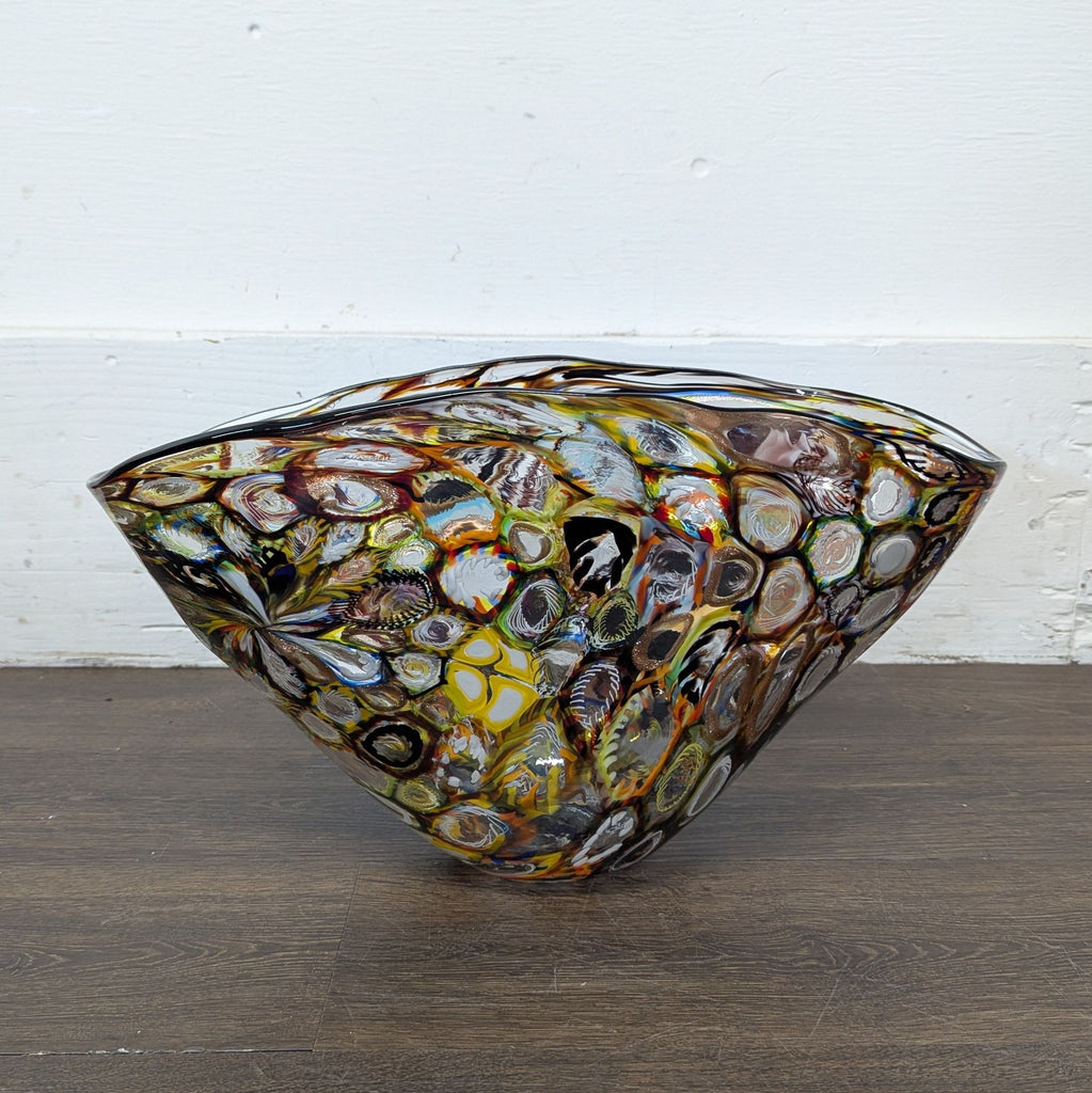 3. Abstract, hand-blown Venetian glass bowl featuring vibrant circular designs on a dark wooden floor.