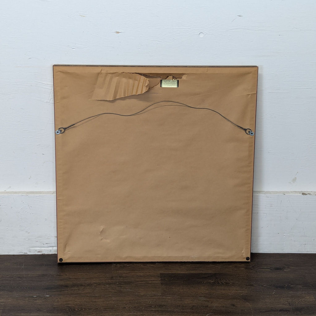 3. Back view of a framed drawing or painting with brown paper backing and hanging wire attached.