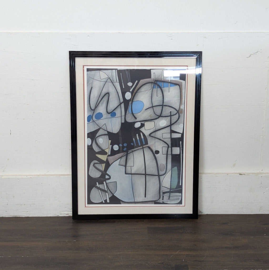 2. Abstract art print with black frame, featuring gray shapes and blue dots, displayed against a white wall.
