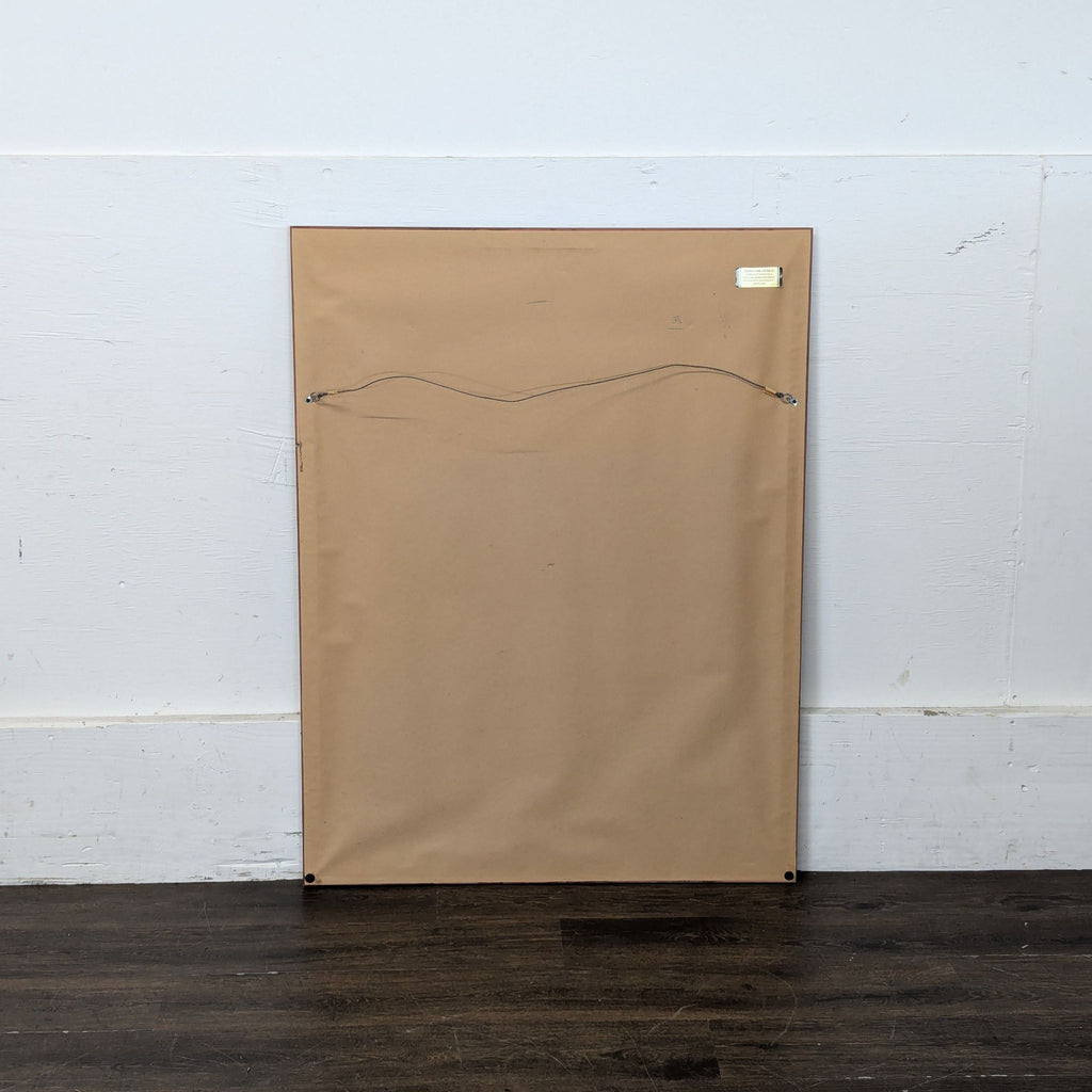 3. Back view of a framed print with brown paper backing and wire for hanging, shown on a wooden floor.