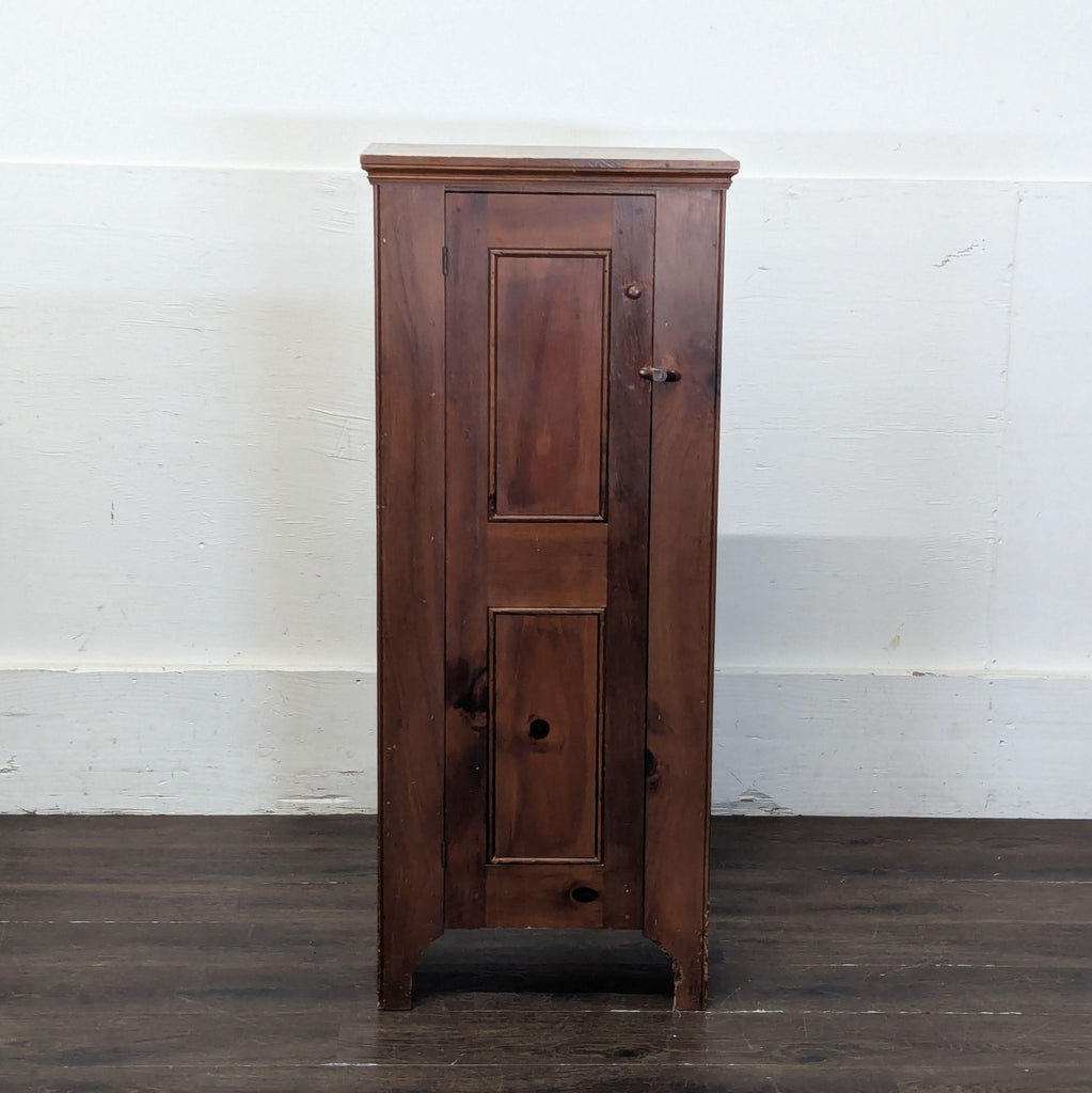 2. Narrow, freestanding wooden cabinet with a simple, paneled door against a white wall.