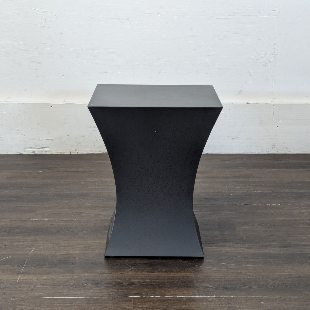 Black metal Room and Board end table with a modern hourglass shape, placed on a dark wood floor.  
