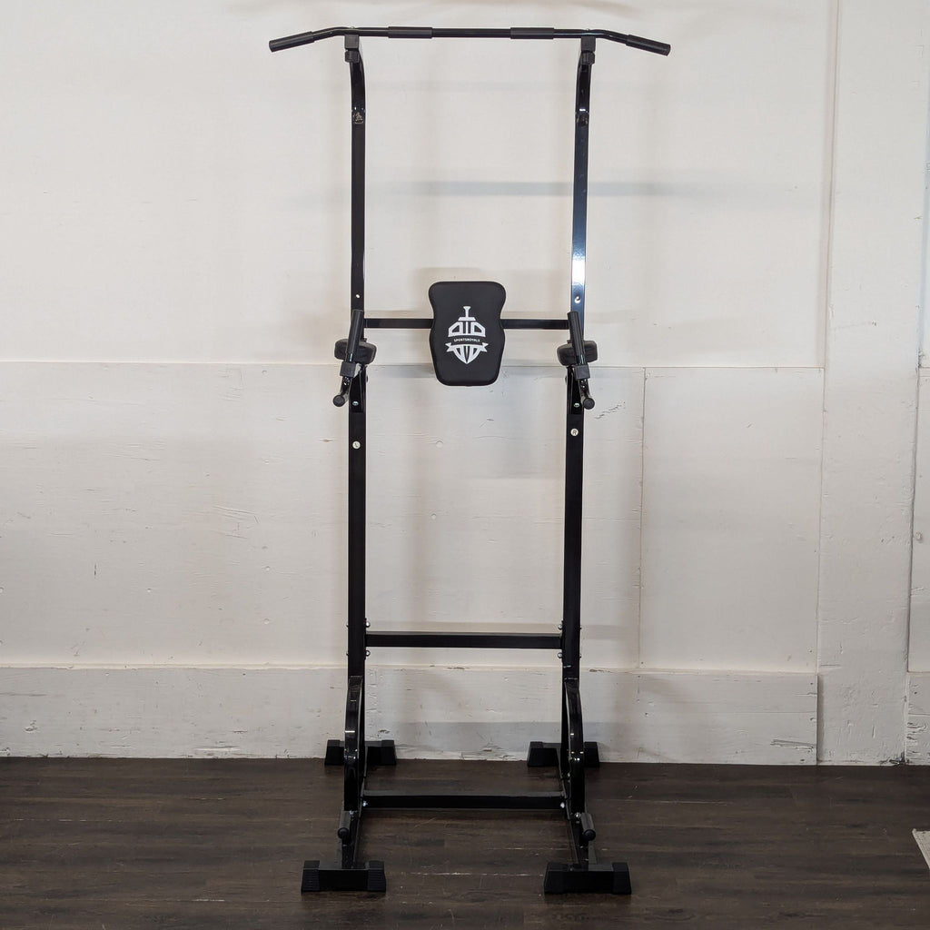 2. Black power tower with pull-up and dip bars, and padded back support, positioned against a white indoor wall.