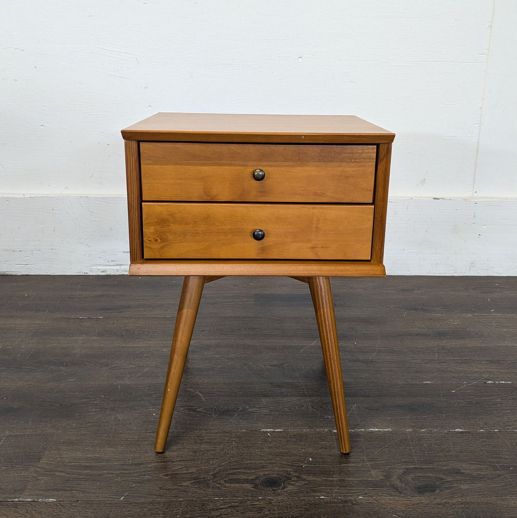 2. Mid-century style wooden end table with two drawers and round black knobs, displayed on dark flooring.