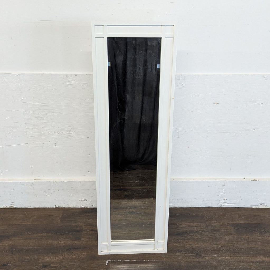 Full-length rectangular Crate & Barrel mirror with a white frame, shown upright against a wall on dark flooring.  