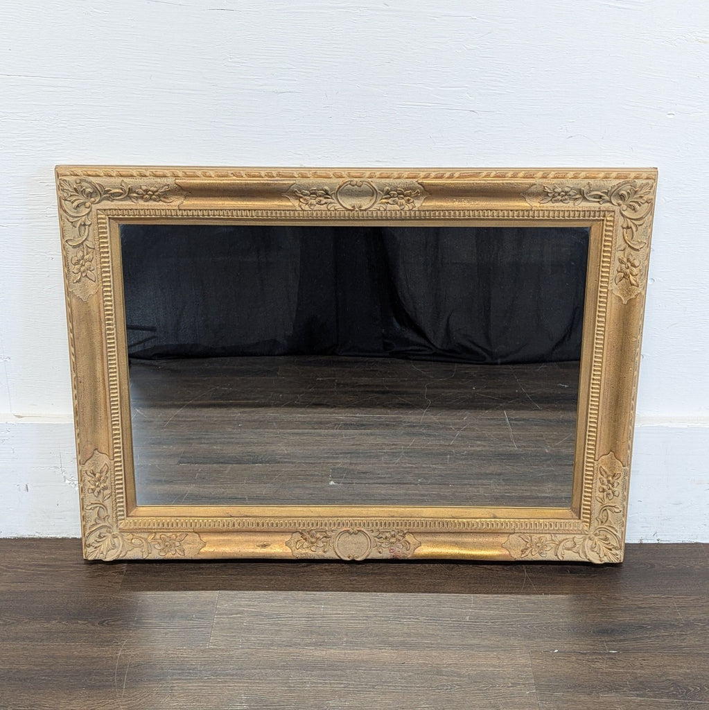 2. Rectangular mirror with a decorative golden frame, propped against a white wall on a dark wooden floor.