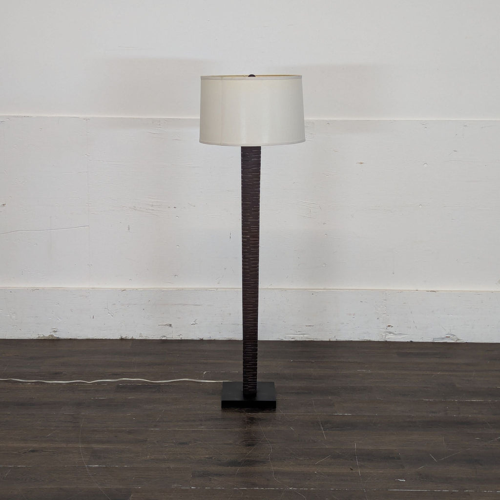 3. Contemporary standing lamp with a sculpted dark base and white shade, placed on a wood floor against a white wall.