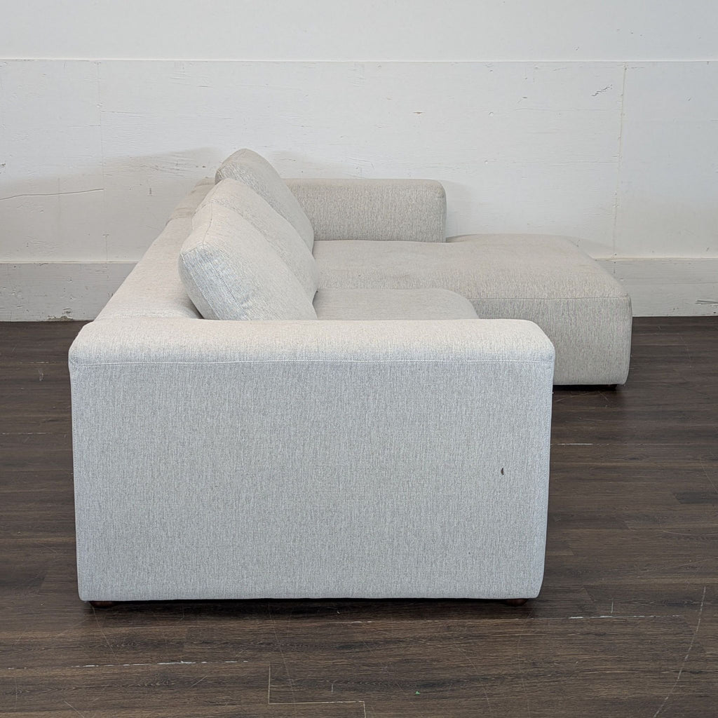 Light gray sectional sofa viewed from the side, showing clean lines and modern design, on a dark wood floor.  