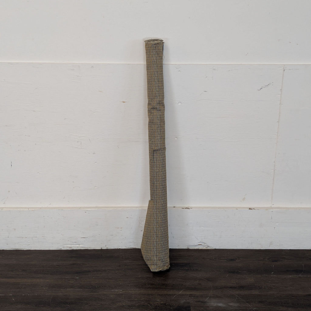 1. Woven fabric-covered object shaped like a bat, propped against a wall on a dark floor.