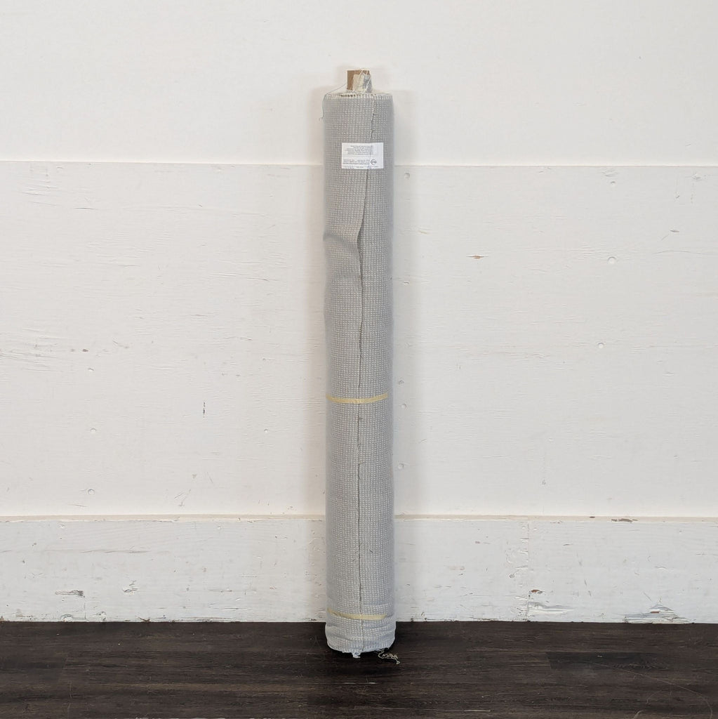 3. A single roll of grey fabric, standing upright against a plain white wall, secured with thin yellow bands.