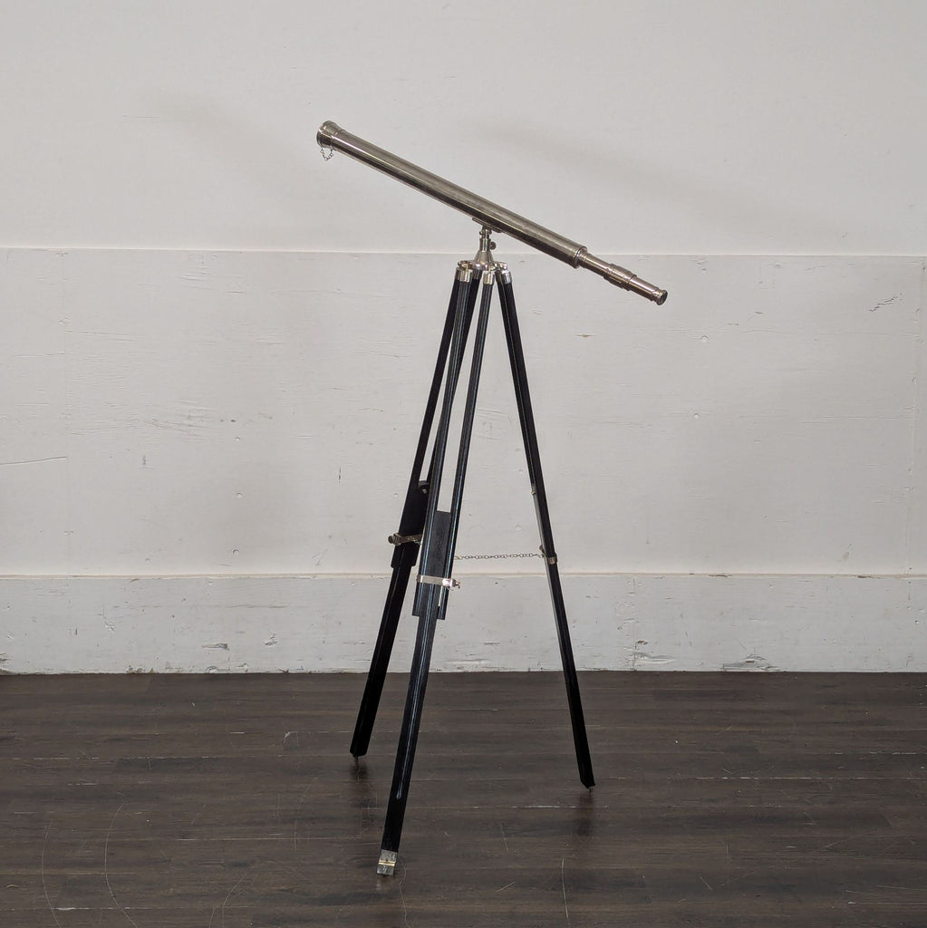 3. Silver telescope on an adjustable black tripod, positioned at an angle in a minimalist indoor setting.