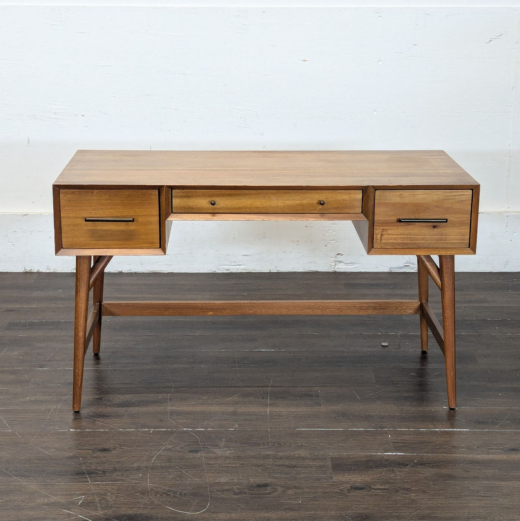 1. Mid-century modern wooden desk with three drawers, tapered legs, and a warm finish, shown against a white wall.