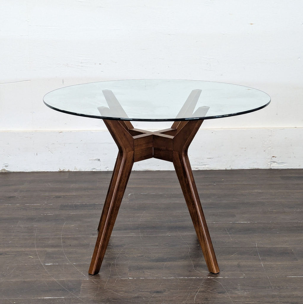 1. Round dining table with a clear glass top and sturdy wooden legs, shown on a dark floor.